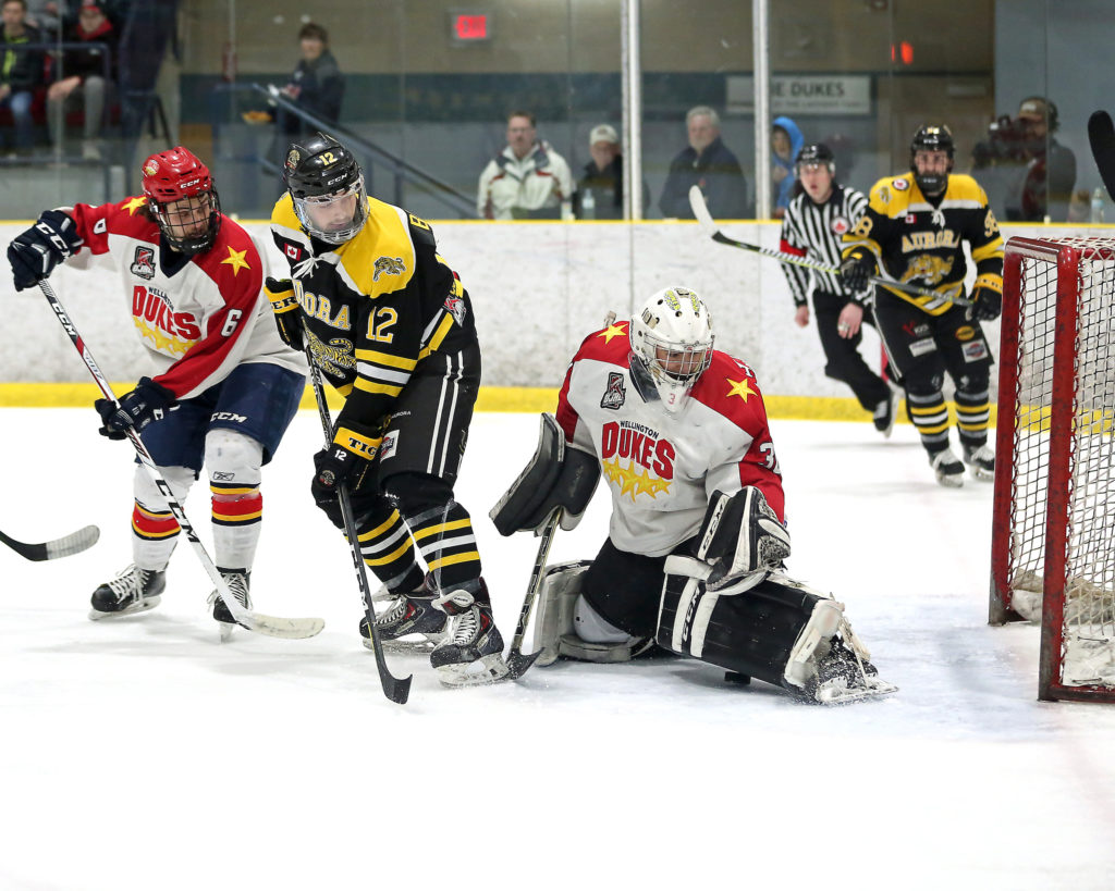 <p>SAVING GRACE- Dukes goalie Jonah Capriotti makes a pad save as defenceman Andrew Barbeau looks to tie up Aurora Tiger forward Evan Bidenti during Wellington’s 6-2 win in Game 2 of the 2018 Buckland Cup Semi-Finals at Essroc Arena Saturday night.<br />
(Photo by Ed McPherson / OJHL Images)</p>
