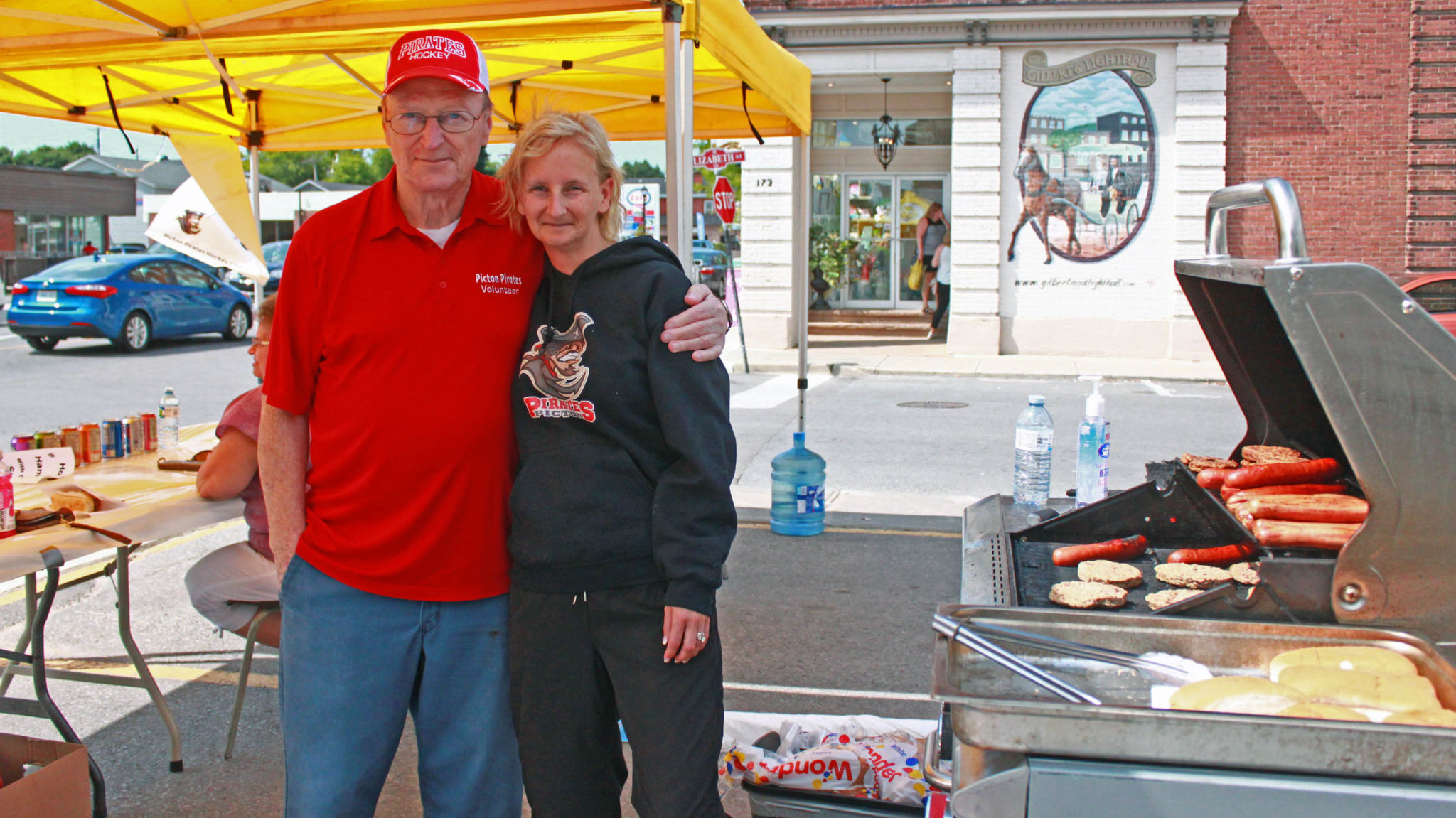 <p>Ross Bull and Tammy Brindley serve burgers, hot dogs, and sausages for the Picton Pirates’ barbecue fundraiser Saturday outside Picton Giant Tiger. (Chad Ibbotson/Gazette staff)</p>
