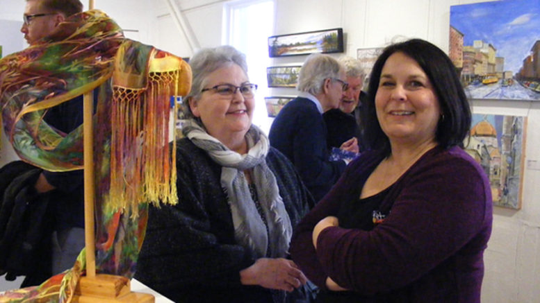 <p>Enjoying artistry – Michelle Sykes (left) from Ancaster and Picton artist Rollande Crawford stand next to a hand-painted silk scarf created by Amélie Koning de Bourbon during the opening reception at Arts on Main Saturday. The new “Spring Colour” show features works from more than 20 artists. (Terry McNamee/For The Gazette)</p>
