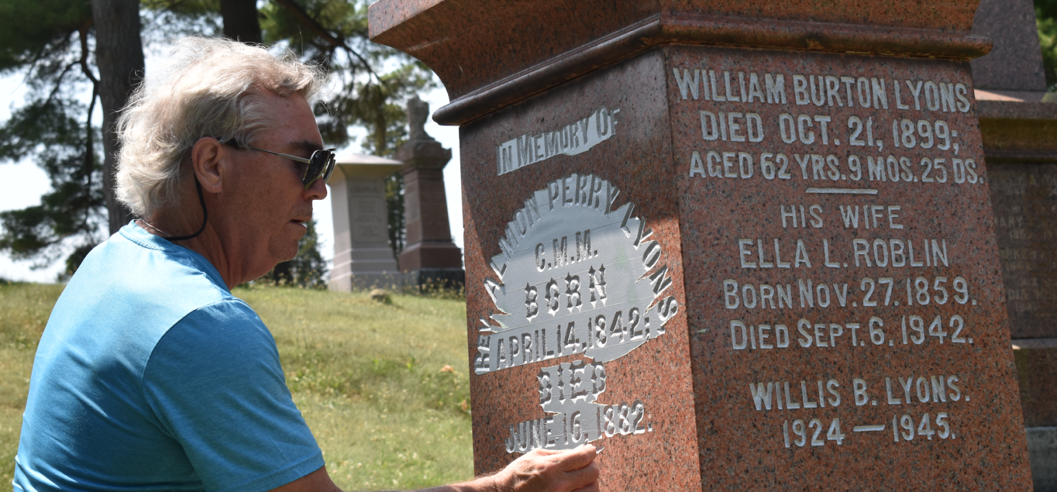 <p>John Lyons peels away covering wax paper to reveal silver inlay on a Lyons family gravestone at Glenwood Cemetery. (Jason Parks/Gazette Staff)</p>
