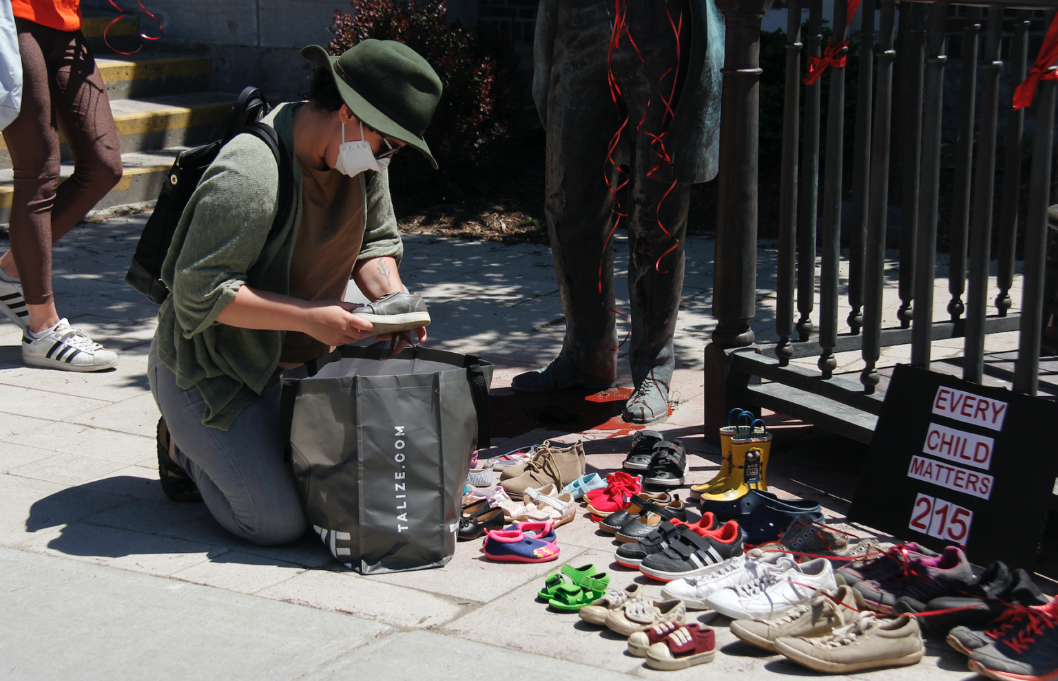 <p>A person lays a pair of children’s shoes at the feet of the Holding Court statue. A vigil remembering the 215 undocumented deaths recently discovered at the Kamloops Residential Schools was hosted in Picton Sunday.  (Desirée Decoste/Gazette staff)</p>
