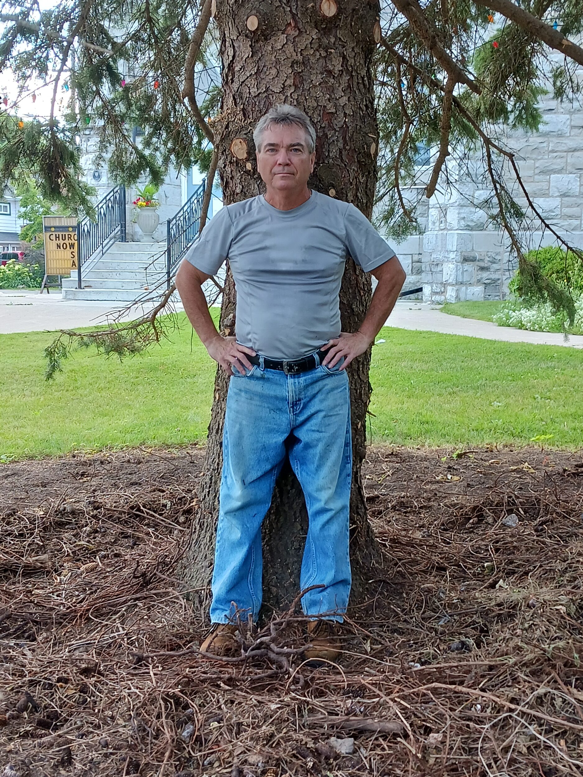 <p>GOOD SAMARITAN- John Lyons stands in front of a stately spruce tree that he is rescuing from the stranglehold of wild grape vines. (Sarah Williams/Gazette Staff)</p>
